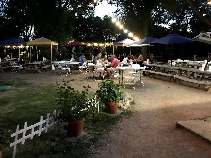 Nighttime view of Bill's Burgers Wings & Things outdoor patio with string lights, picnic tables, and seated diners.